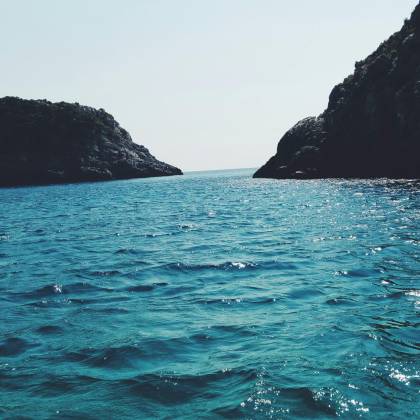 Breathtaking View Of A Serene Ocean With Distant Rocky Cliffs Under A Clear Sky.