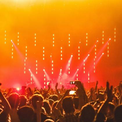 Energetic Crowd At A Live Concert With Bright Stage Lights And Hands Raised In Celebration.