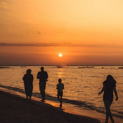 A Family Walking Along Mandra Beach, Greece, Silhouetted Against A Stunning Sunset.