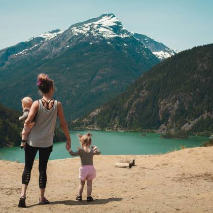 A Mother With Two Children Enjoys A Scenic Mountain And Lake View During A Sunny Outdoor Hike.