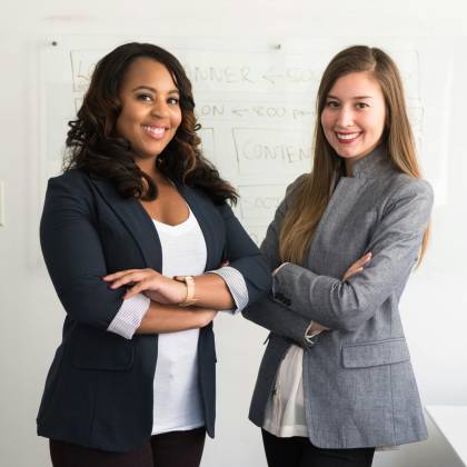 Two Diverse Businesswomen Smiling Confidently In A Modern Office Environment.