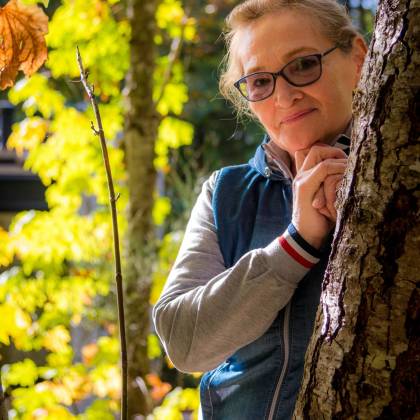 Smiling Senior Woman With Glasses Enjoys A Sunny Autumn Day Outdoors Near A Tree.