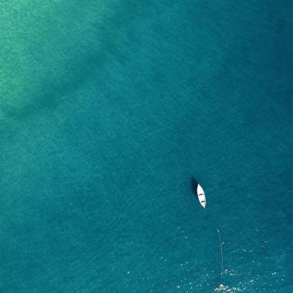 Aerial View Of A Lone Boat On Calm Turquoise Waters, Showcasing Tranquility.