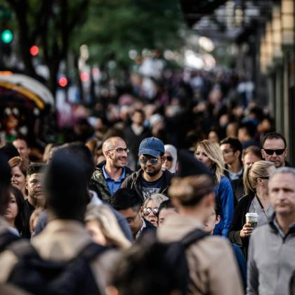 A Bustling Urban Scene With Diverse People Walking On A Tree Lined City Street.