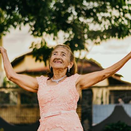 Elderly Woman In A Pink Lace Dress Smiling And Posing Outdoors.