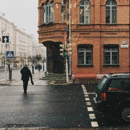 A Pedestrian Walks On A Snow Covered Street Corner By A Historic Brick Building In Winter.