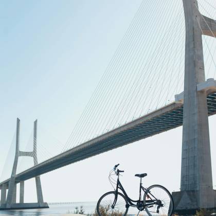 A Bicycle With Vibrant Graffiti Beneath A Striking Suspension Bridge Under A Clear Blue Sky.