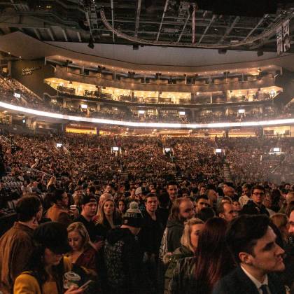 A Large Crowd Gathers In An Indoor Arena For A Lively Event, Surrounded By Bright Lights.