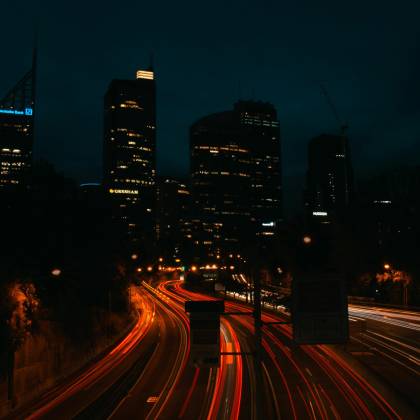 Urban Night Scene Capturing Light Trails On A Highway Under A Dark Sky, Showcasing City Skyscrapers.