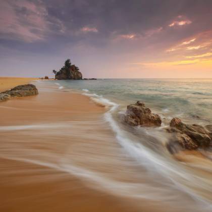 Tranquil Beach Scene At Sunrise With Soft Waves And Rock Formations.