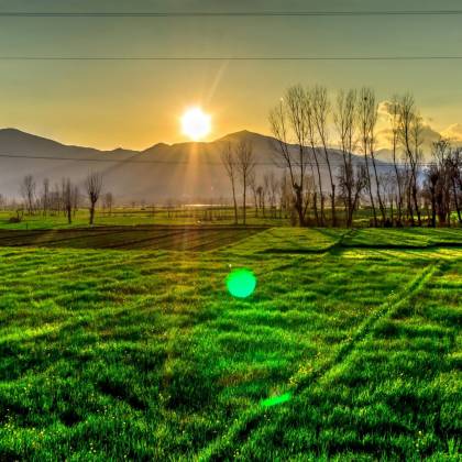 Golden Sunrise Over Green Fields In Kalam, Pakistan, With Distant Mountains And Serene Landscape.