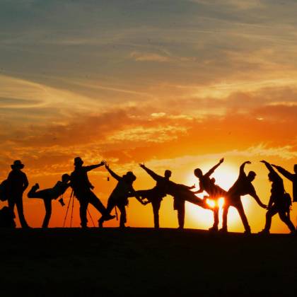 Group Of People Silhouetted Against A Vibrant Sunset, Showcasing Unity And Joy.