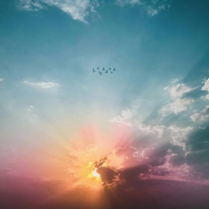 A Breathtaking View Of A Sunset Sky With Clouds And A Flock Of Birds Flying Across.