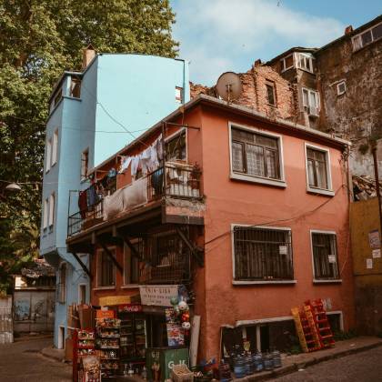 Colorful Urban Street Scene Featuring A Corner Shop, Vibrant Buildings, And Laundry Lines Under A Clear Sky.