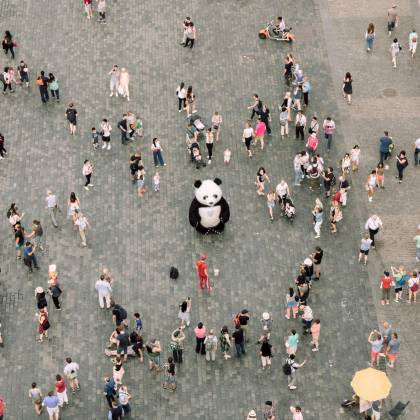 Aerial Shot Of A Bustling City Square With A Panda Mascot And Street Performers Engaging A Crowd.