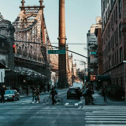 People And Vehicles At A Bustling New York City Intersection Near The Iconic Queensboro Bridge.
