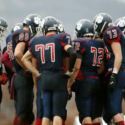 American Football Players In A Huddle Planning Their Next Move On A Grassy Field.