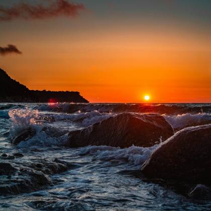 Dramatic Sunset Over Ocean Waves Crashing Onto Rocky Shore. Perfect For Serene And Nature Themed Content.
