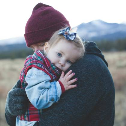 A Father And Child Embrace Outdoors With A Winter Mountain Backdrop.
