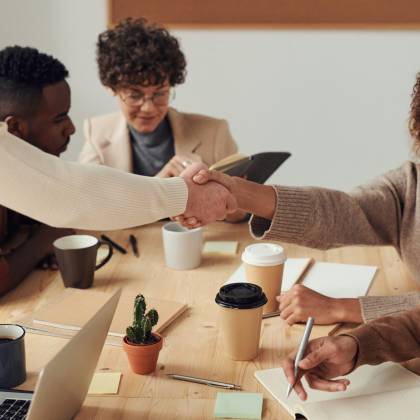 Colleagues Collaborating Indoors, Sharing Smiles, And Shaking Hands During A Business Meeting.