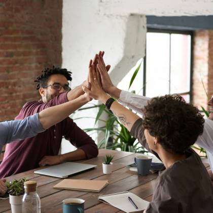 Diverse Group Of Professionals Giving A High Five In An Office Setting, Symbolizing Teamwork And Success.