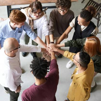 A Diverse Group Of Professionals Joins Hands In A Team Building Exercise Indoors.