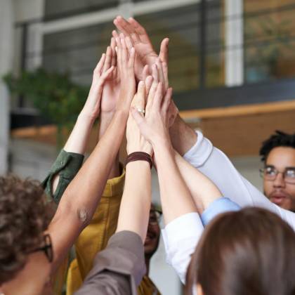 A Group Of Diverse Professionals Celebrating Teamwork With A High Five Indoors.