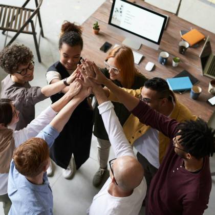 A Diverse Group Of Colleagues Giving A High Five During A Corporate Meeting Indoors.