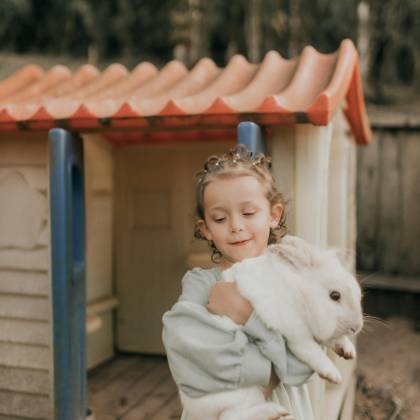 A Young Girl Lovingly Embraces A Rabbit Near A Playhouse Outdoors.
