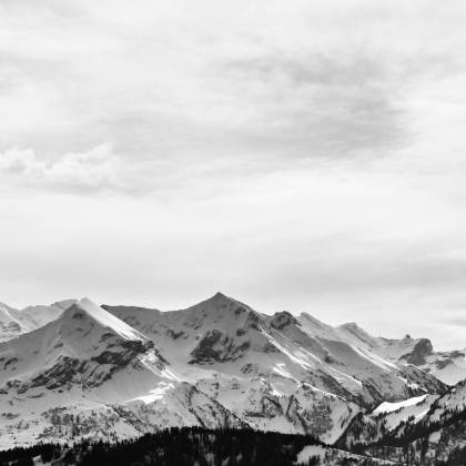 Stunning Monochrome Landscape Of Snow Covered Alpine Mountains Under A Cloudy Sky.