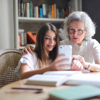 A Grandmother And Granddaughter Bonding Over A Smartphone At Home, Showcasing Generational Connection.