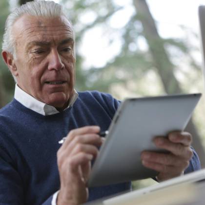 Elderly Man Focused On Using A Tablet In A Natural Outdoor Setting.