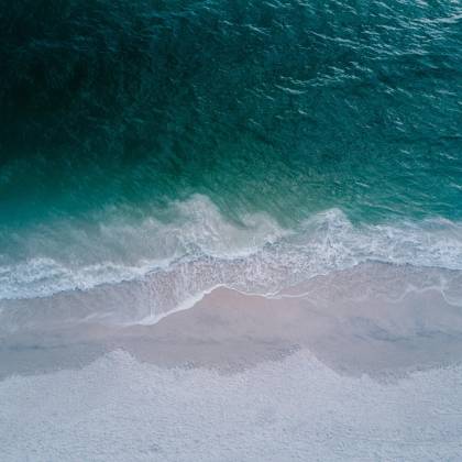 Stunning Aerial Shot Of Turquoise Ocean Waves Washing Onto A Pristine Sandy Beach, Perfect For Backgrounds.