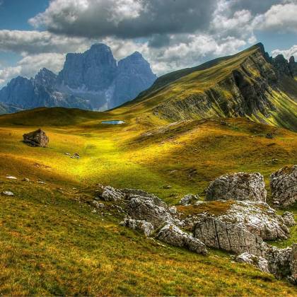 Explore A Stunning Alpine Landscape With Rolling Hills And Majestic Mountains Under A Cloudy Sky.