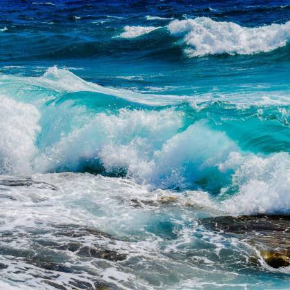 Vibrant Blue Ocean Waves Crashing Against Rocky Shoreline Under Clear Summer Skies.