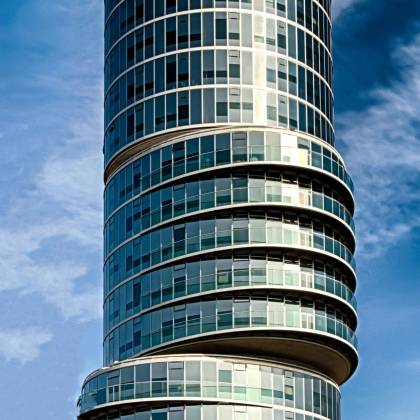 Low Angle View Of A Modern Glass Skyscraper Against A Blue Sky, Showcasing Futuristic Architecture.