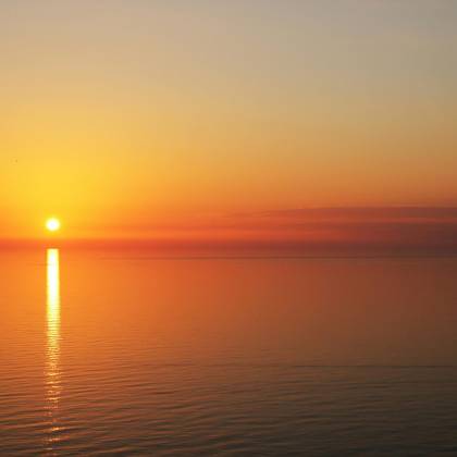 A Tranquil Sunset Over Calm Ocean Waters With Golden Reflections In The Sky And Sea.