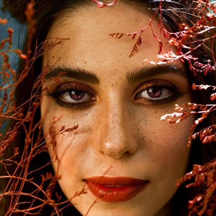 Striking Close Up Portrait Of A Woman Framed By Vibrant Red Leaves, Showcasing Natural Beauty And Expression.