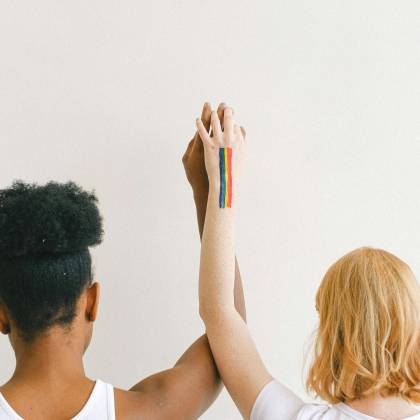 An Interracial Couple Showing Unity And Pride With Raised Arms And A Rainbow Tattoo.