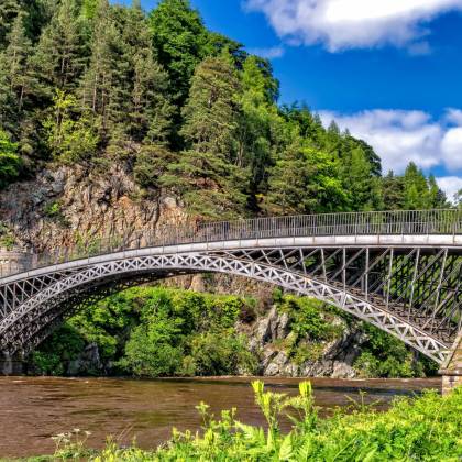 Scenic View Of A Historic Bridge Amidst Lush Greenery And Rocky Cliffs.
