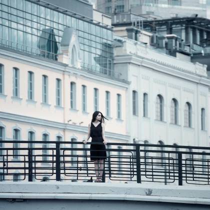 Woman In Black Dress Standing On A Bridge Against A Modern Cityscape Background.
