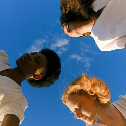 Three Women Holding Hands Under A Clear Blue Sky, Symbolizing Unity And Friendship.