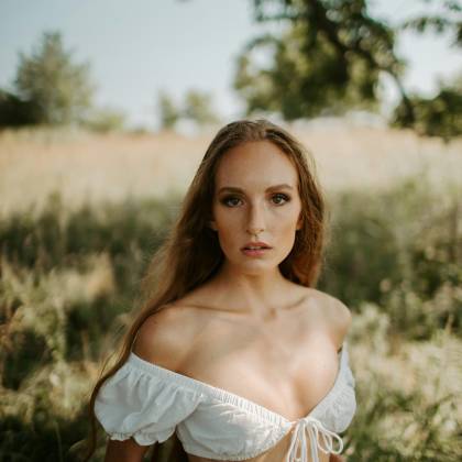 A Serene Portrait Of A Woman In A White Top In A Sunny Meadow, Exuding Natural Beauty.