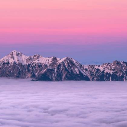 Breathtaking View Of A Snow Covered Mountain Peak Rising Above Clouds During A Stunning Pink Sunrise.