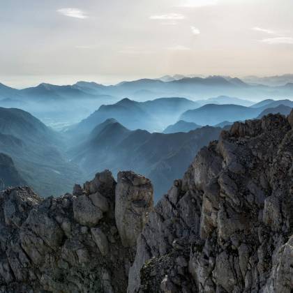 Capture Of A Tranquil Mountain Range At Dawn With Misty Valleys And Rocky Peaks.