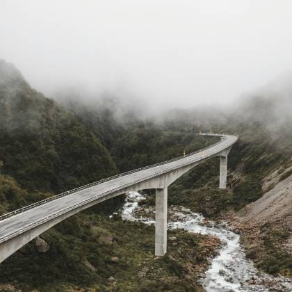 Scenic View Of A Bridge Over A River In A Foggy Mountain Landscape, Capturing Nature's Beauty.