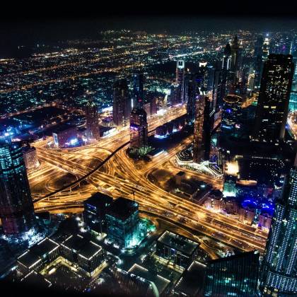 A Stunning Aerial View Of Dubai's Illuminated Skyline At Night, Showcasing Its Modern Architecture And Busy Roads.