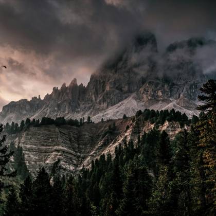 Breathtaking View Of The Dolomites Under Dramatic Skies And Dense Forest, Creating A Picturesque Landscape.
