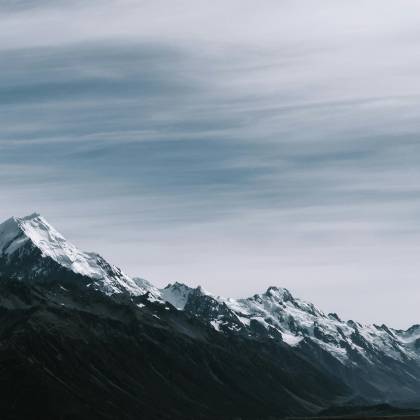 Breathtaking View Of Snow Capped Mountain Peaks Under A Cloudy Sky.