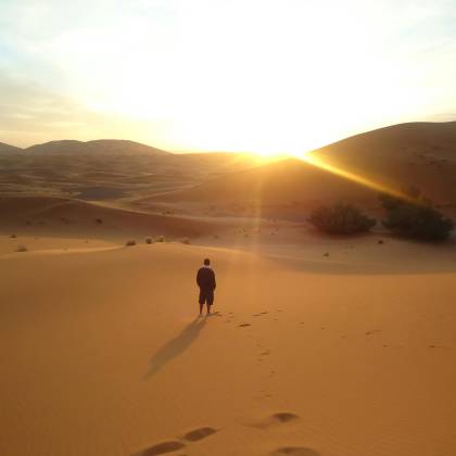 Silhouette Of A Man Walking Along Sand Dunes During A Sunrise In The Sahara Desert.